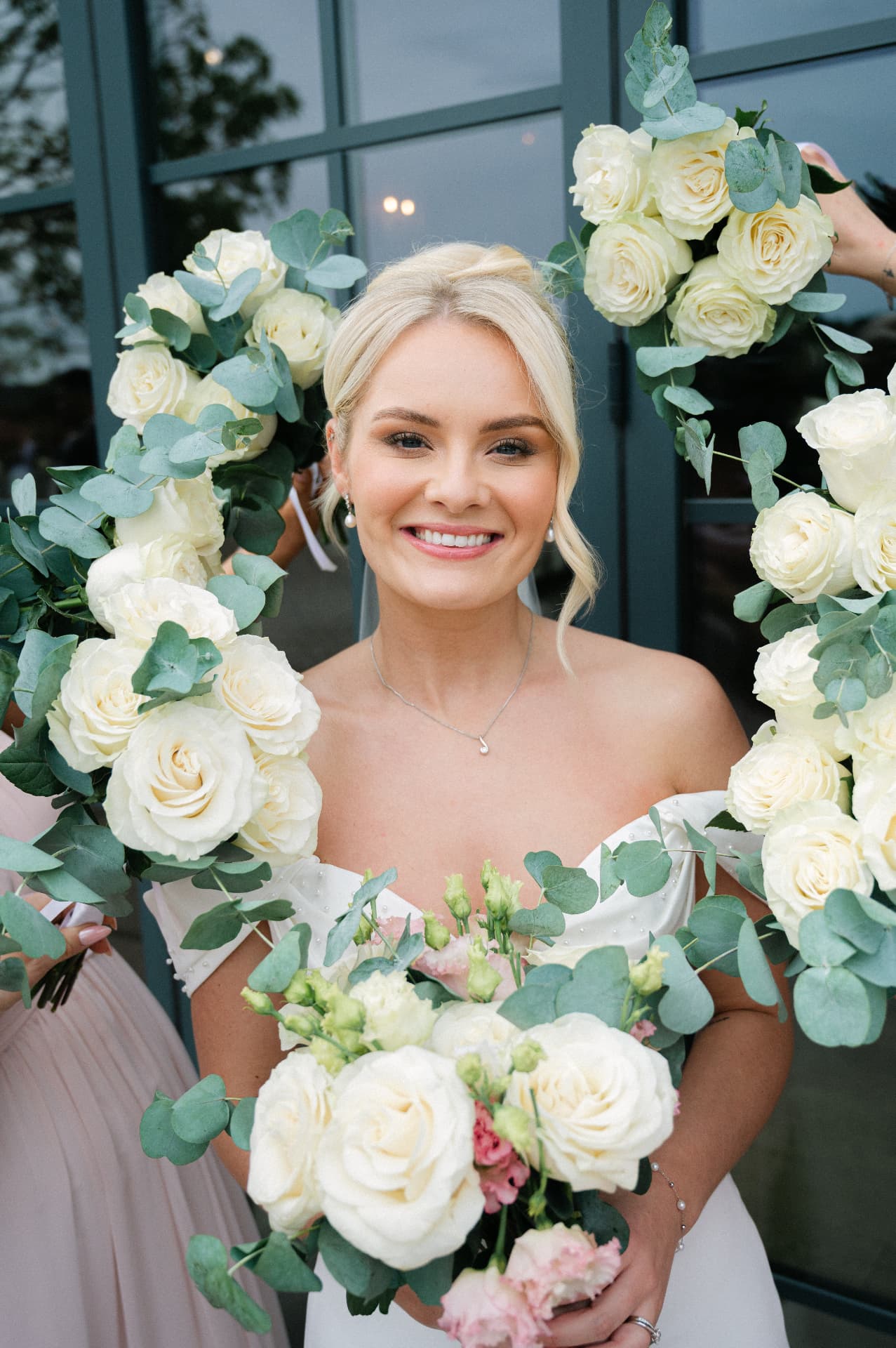 Bride smiling with her bouquet framed by eucalyptus and white roses